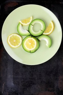 Avokado ve limon bir yeşil plaka, karanlık bir antika arka plan, Vejetaryen gıda, sağlıklı doğal gıda, tropik meyveler avokado kahvaltı için dilimlenmiş, kopyalama alanı