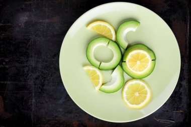 Avokado ve limon bir yeşil plaka, karanlık bir antika arka plan, Vejetaryen gıda, sağlıklı doğal gıda, tropik meyveler avokado kahvaltı için dilimlenmiş, kopyalama alanı