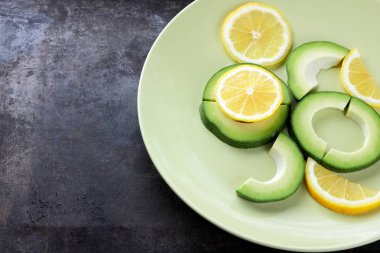 Avokado ve limon bir yeşil plaka, karanlık bir antika arka plan, Vejetaryen gıda, sağlıklı doğal gıda, tropik meyveler avokado kahvaltı için dilimlenmiş, kopyalama alanı