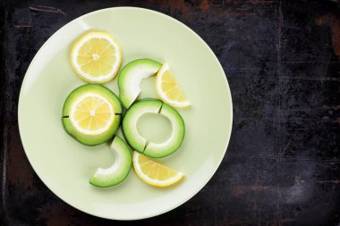 Avokado ve limon bir yeşil plaka, karanlık bir antika arka plan, Vejetaryen gıda, sağlıklı doğal gıda, tropik meyveler avokado kahvaltı için dilimlenmiş, kopyalama alanı