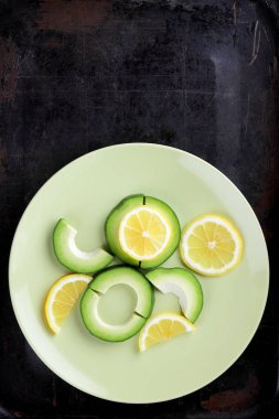 Avokado ve limon bir yeşil plaka, karanlık bir antika arka plan, Vejetaryen gıda, sağlıklı doğal gıda, tropik meyveler avokado kahvaltı için dilimlenmiş, kopyalama alanı