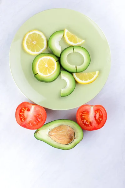 Sliced avocado and lemons on a green plate, avocado on white background, vegetarian food, useful natural food, tropical fruits for breakfast, copy space