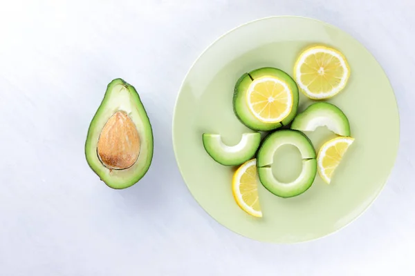 Sliced avocado and lemons on a green plate, avocado on white background, vegetarian food, useful natural food, tropical fruits for breakfast, copy space