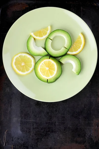 Avokado ve limon bir yeşil plaka, karanlık bir antika arka plan, Vejetaryen gıda, sağlıklı doğal gıda, tropik meyveler avokado kahvaltı için dilimlenmiş, kopyalama alanı