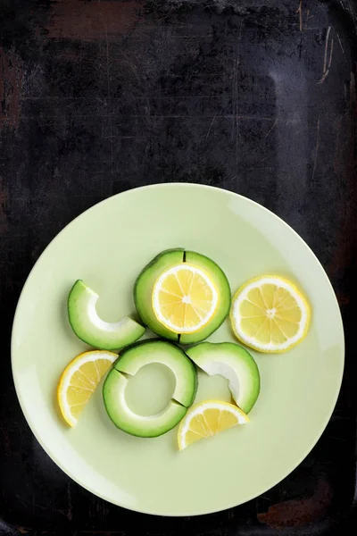 Avokado ve limon bir yeşil plaka, karanlık bir antika arka plan, Vejetaryen gıda, sağlıklı doğal gıda, tropik meyveler avokado kahvaltı için dilimlenmiş, kopyalama alanı