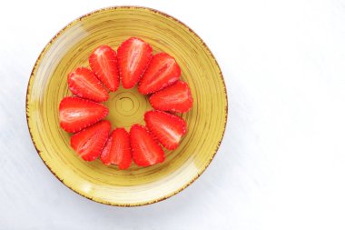 Sarı bir tabak, çizgili kırmızı çilek yarım daire üstten görünüm, beyaz bir arka planda, vejetaryen yemek kahvaltı için kırmızı çilek çilek kopyalama alanı, sağlıklı gıda, diyet