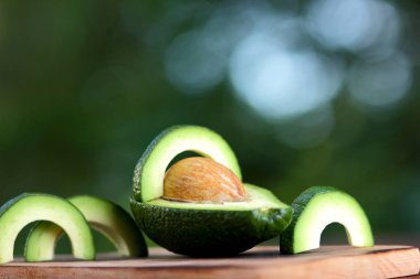 Avokado bulanık yeşil bokeh arka planda, bir ahşap masa, egzotik meyve salatası, vejetaryen yemek, Meksika yemeği, kopya alanı için üzerinde kesme avokado