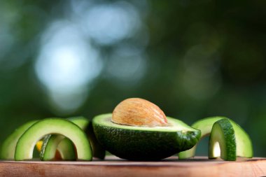 Avokado bulanık yeşil bokeh arka planda, bir ahşap masa, egzotik meyve salatası, vejetaryen yemek, Meksika yemeği, kopya alanı için üzerinde kesme avokado