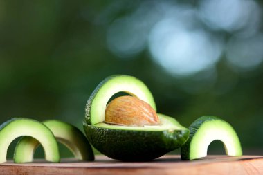 Avokado bulanık yeşil bokeh arka plan, bir ahşap masa, egzotik meyve salatası, vejetaryen yemek, Meksika yemeği, organik, üzerinde kesme avokado kopyalama alanı