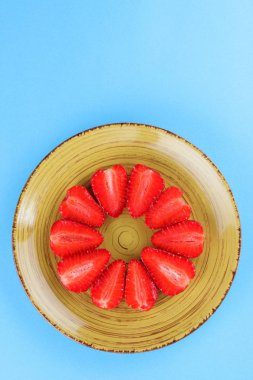 Alan, bir tasarımcı için yaratıcı boş çilek mavi arka plan, bir daire, vejetaryen yemek kahvaltı için sarı bir tabakta kırmızı meyveler şeklinde kırmızı çilek yarısı üzerinde kopyalama