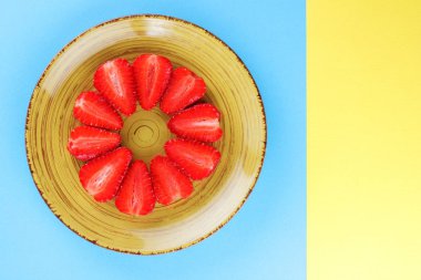 Alan, bir tasarımcı için yaratıcı boş çilek mavi arka plan, bir daire, vejetaryen yemek kahvaltı için sarı bir tabakta kırmızı meyveler şeklinde kırmızı çilek yarısı üzerinde kopyalama