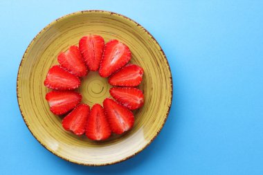 Alan, bir tasarımcı için yaratıcı boş çilek mavi arka plan, bir daire, vejetaryen yemek kahvaltı için sarı bir tabakta kırmızı meyveler şeklinde kırmızı çilek yarısı üzerinde kopyalama