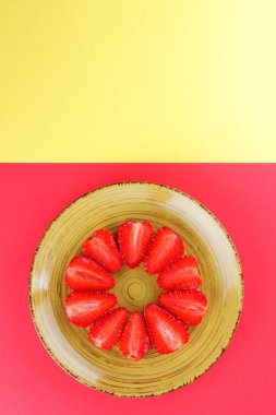 Çilek kırmızı bir arka plan, bir daire, vejetaryen yemek kahvaltı için sarı bir tabakta kırmızı meyveler şeklinde kırmızı çilek yarısı Tarih alanı, bir tasarımcı için yaratıcı boş kopyalama