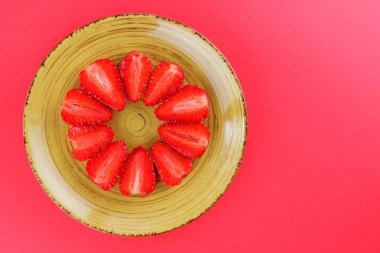 Çilek kırmızı bir arka plan, bir daire, vejetaryen yemek kahvaltı için sarı bir tabakta kırmızı meyveler şeklinde kırmızı çilek yarısı Tarih alanı, bir tasarımcı için yaratıcı boş kopyalama