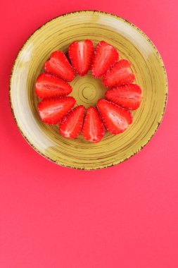 Çilek kırmızı bir arka plan, bir daire, vejetaryen yemek kahvaltı için sarı bir tabakta kırmızı meyveler şeklinde kırmızı çilek yarısı Tarih alanı, bir tasarımcı için yaratıcı boş kopyalama