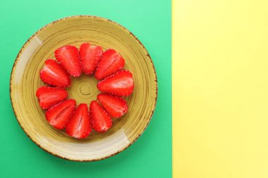 Çilek yeşil bir arka planda bir daire, vejetaryen yemek kahvaltı için sarı bir tabakta kırmızı meyveler şeklinde kırmızı çilek yarısı alanı, bir tasarımcı için yaratıcı boş kopyalama