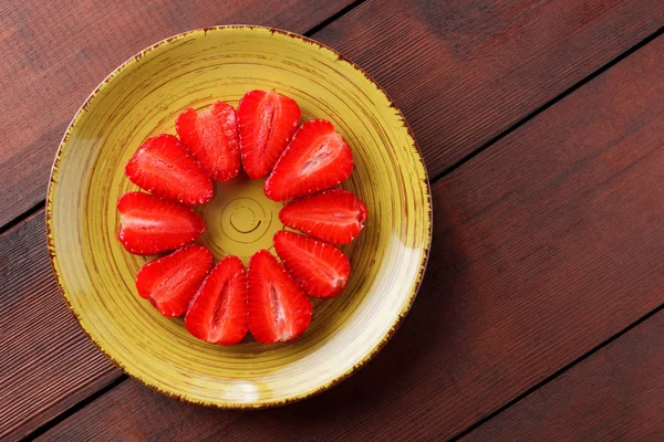 Strawberries on wooden boards, halves of red strawberry in the form of a circle, red berries on a yellow plate, vegetarian food for breakfast, copy space, blank for a designer, creative