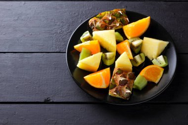 Ahşap panoları, ananas, portakal ve kivi karanlık bir arka plan üzerinde Kahvaltı, vejetaryen yemek, kopya alanı için kıyılmış tropikal meyve salatası üzerinde siyah bir plaka üzerinde meyve salatası