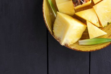 Ahşap kurullarında sarı bir tabağa ananas parçaları, koyu arka plan, tropikal meyve salatası ananas meyve yeşil yaprakları Kahvaltı, vejetaryen yemek, kopya alanı için