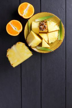 Ananas ve ahşap panoları, ananas meyve ve portakal karanlık bir arka plan, tropikal meyve salatası kahvaltıda vejetaryen yemek, üzerinde sarı bir plaka üzerinde yarım portakal parçaları alanı Kopyala