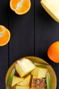 Ananas ve ahşap panoları, ananas meyve ve portakal karanlık bir arka plan, tropikal meyve salatası kahvaltıda vejetaryen yemek, üzerinde sarı bir plaka üzerinde yarım portakal parçaları alanı Kopyala