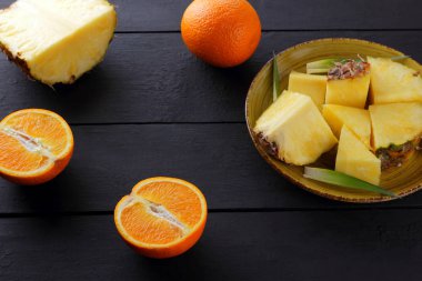 Ananas ve ahşap panoları, ananas meyve ve portakal karanlık bir arka plan, tropikal meyve salatası kahvaltıda vejetaryen yemek, üzerinde sarı bir plaka üzerinde yarım portakal parçaları alanı Kopyala