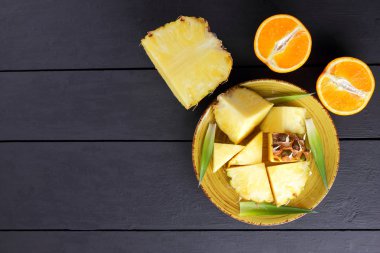 Ananas ve ahşap panoları, ananas meyve ve portakal karanlık bir arka plan, tropikal meyve salatası kahvaltıda vejetaryen yemek, üzerinde sarı bir plaka üzerinde yarım portakal parçaları alanı Kopyala