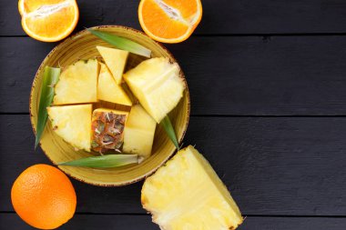 Ananas ve ahşap panoları, ananas meyve ve portakal karanlık bir arka plan, tropikal meyve salatası kahvaltıda vejetaryen yemek, üzerinde sarı bir plaka üzerinde yarım portakal parçaları alanı Kopyala