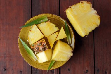 Ahşap kurullarında sarı bir tabağa ananas parçaları, ahşap zemin, Kahvaltı, vejetaryen yemek, kopya alanı için tropikal meyve salatası ananas ile yeşil yaprakları