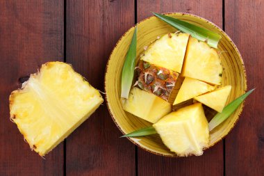 Ahşap kurullarında sarı bir tabağa ananas parçaları, ahşap zemin, Kahvaltı, vejetaryen yemek, kopya alanı için tropikal meyve salatası ananas ile yeşil yaprakları