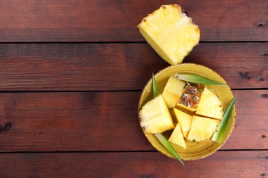 Ahşap kurullarında sarı bir tabağa ananas parçaları, ahşap zemin, Kahvaltı, vejetaryen yemek, kopya alanı için tropikal meyve salatası ananas ile yeşil yaprakları