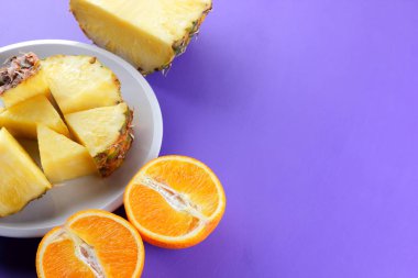 Ananas ve portakal beyaz bir tabak, doğranmış ananas ve menekşe arka plan, tropikal meyveler kahvaltıda vejetaryen yemek, salata üzerinde yarım portakal parçaları alanı Kopyala