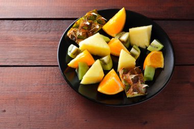 Meyve salatası vegans, ananas, portakal ve kivi siyah bir plaka üzerinde ahşap panoları, narenciye salatası üstten görünüm, kopya alanı tropikal meyve parçaları için