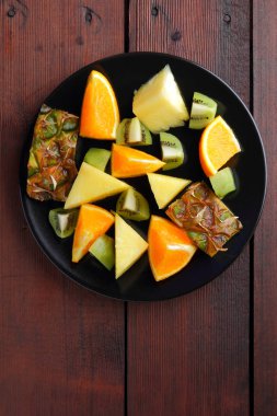 Meyve salatası vegans, ananas, portakal ve kivi siyah bir plaka üzerinde ahşap panoları, narenciye salatası üstten görünüm, kopya alanı tropikal meyve parçaları için