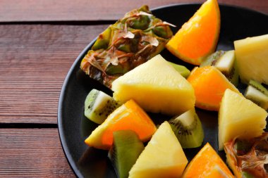Meyve salatası vegans, ananas, portakal ve kivi siyah bir plaka üzerinde ahşap panoları, narenciye salatası üstten görünüm, kopya alanı tropikal meyve parçaları için
