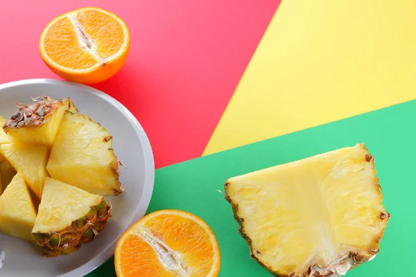 Pieces of pineapple and oranges on a white plate, chopped pineapple and half orange on a colorful background, tropical fruit salad in pop art style, vegetarian food