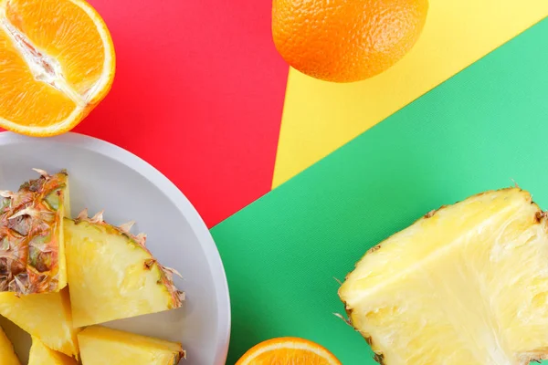 Pieces of pineapple and oranges on a white plate, chopped pineapple and half orange on a colorful background, tropical fruit salad in pop art style, vegetarian food