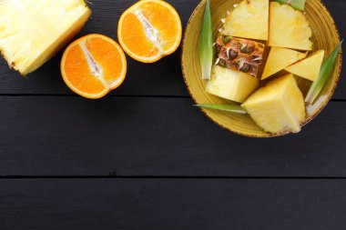 Ananas ve ahşap panoları, ananas meyve ve karanlık bir arka planda tropikal meyve salatası kahvaltıda portakal üzerinde sarı bir plaka üzerinde yarım portakal parçaları