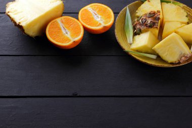 Ananas ve ahşap panoları, ananas meyve ve karanlık bir arka planda tropikal meyve salatası kahvaltıda portakal üzerinde sarı bir plaka üzerinde yarım portakal parçaları