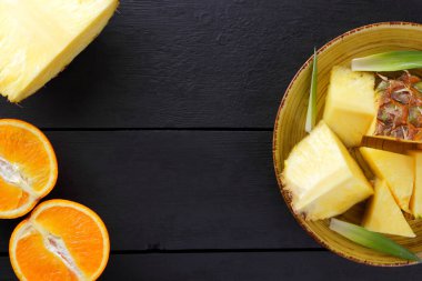 Ananas ve ahşap panoları, ananas meyve ve karanlık bir arka planda tropikal meyve salatası kahvaltıda portakal üzerinde sarı bir plaka üzerinde yarım portakal parçaları