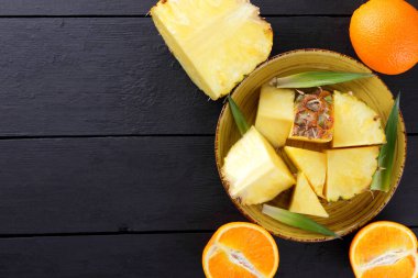 Ananas ve ahşap panoları, ananas meyve ve karanlık bir arka planda tropikal meyve salatası kahvaltıda portakal üzerinde sarı bir plaka üzerinde yarım portakal parçaları