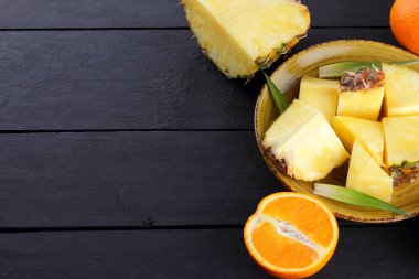Ananas ve ahşap panoları, ananas meyve ve karanlık bir arka planda tropikal meyve salatası kahvaltıda portakal üzerinde sarı bir plaka üzerinde yarım portakal parçaları