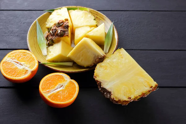 Ananas ve ahşap panoları, ananas meyve ve karanlık bir arka planda tropikal meyve salatası kahvaltıda portakal üzerinde sarı bir plaka üzerinde yarım portakal parçaları