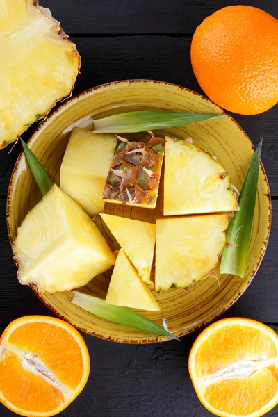 Ananas ve ahşap panoları, ananas meyve ve karanlık bir arka planda tropikal meyve salatası kahvaltıda portakal üzerinde sarı bir plaka üzerinde yarım portakal parçaları