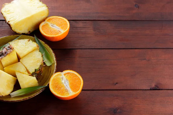 Ananas ve portakal ahşap panoları, ananas ve portakal ahşap zemin, kahvaltı için tropikal meyve salatası yarısı sarı bir plaka üzerinde parçalar