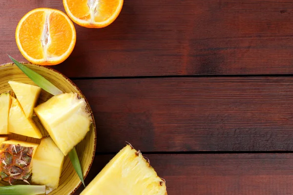 Ananas ve portakal ahşap panoları, ananas ve portakal ahşap zemin, kahvaltı için tropikal meyve salatası yarısı sarı bir plaka üzerinde parçalar
