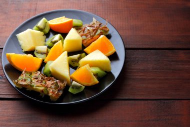 Meyve salatası vegans, ananas, portakal ve kivi siyah bir plaka üzerinde ahşap panoları, narenciye salatası üstten görünüm, vejetaryen yemek tropikal meyve parçaları için
