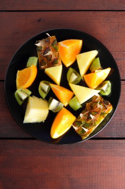 Meyve salatası vegans, ananas, portakal ve kivi siyah bir plaka üzerinde ahşap panoları, narenciye salatası üstten görünüm, vejetaryen yemek tropikal meyve parçaları için
