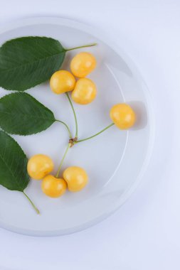 Sarı kiraz taze kiraz beyaz bir arka plan, sarı çilek minimalizm tarzı, vejetaryen yemek, tasarımcı, boş beyaz bir tabakta yeşil yaprakları ile izole