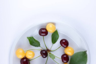 Beyaz bir tabak, yeşil yaprakları ile çok renkli taze kiraz, Minimalizm, vejetaryen yemek, boş Tasarımcısı tarzında sarı ve kırmızı çilek kırmızı ve Sarı kiraz